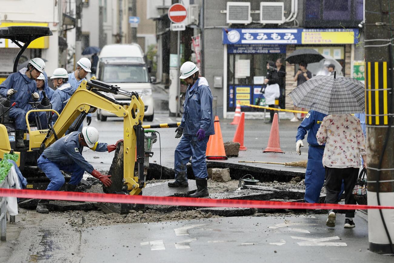 マンホールから水が噴き出してひび割れた道路の復旧作業＝26日午前10時5分、大阪市生野区（共同）