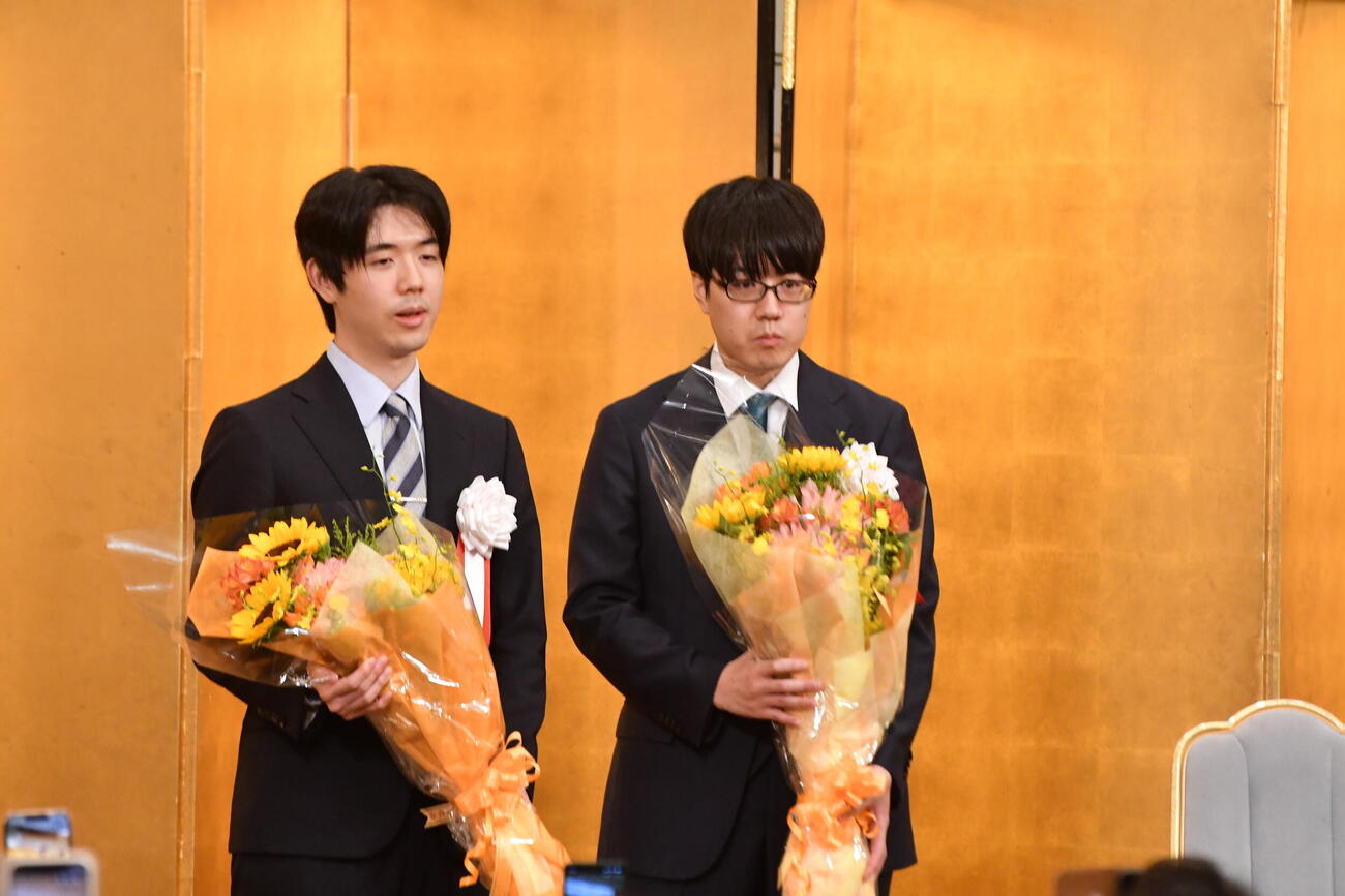 棋聖戦第3局前夜祭で地元の女子高生から贈られた花束を手にする藤井聡太棋聖（左）と服部慎一郎七段（右）
