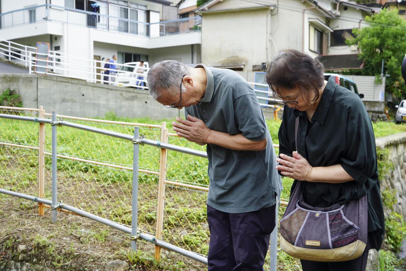 大規模土石流で全壊した自宅跡付近で手を合わせる太田滋さん（左）＝3日午前、静岡県熱海市(共同)