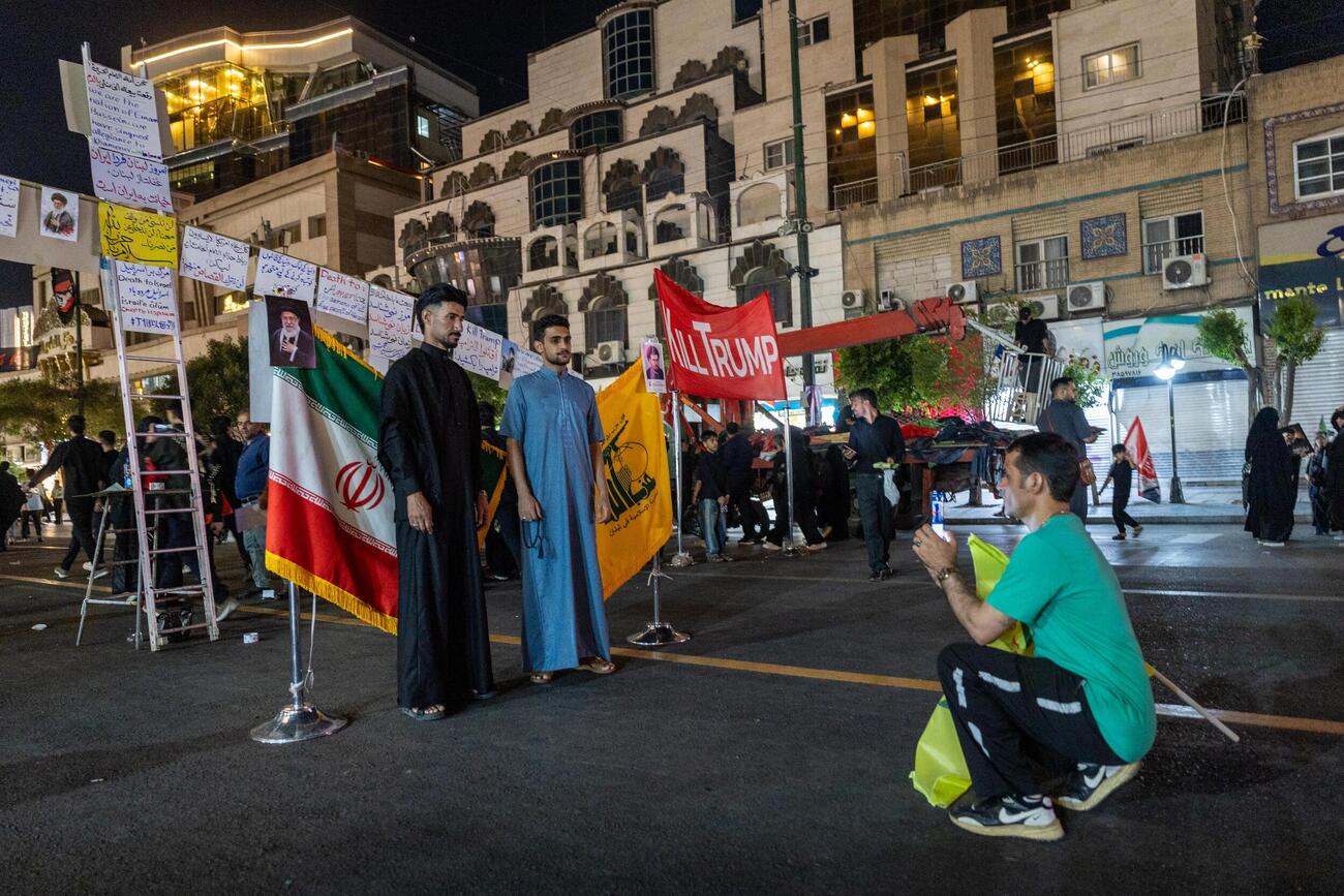 イラン北東部マシャドで、イラン国旗とヒズボラの旗の前で記念撮影する人々（共同）