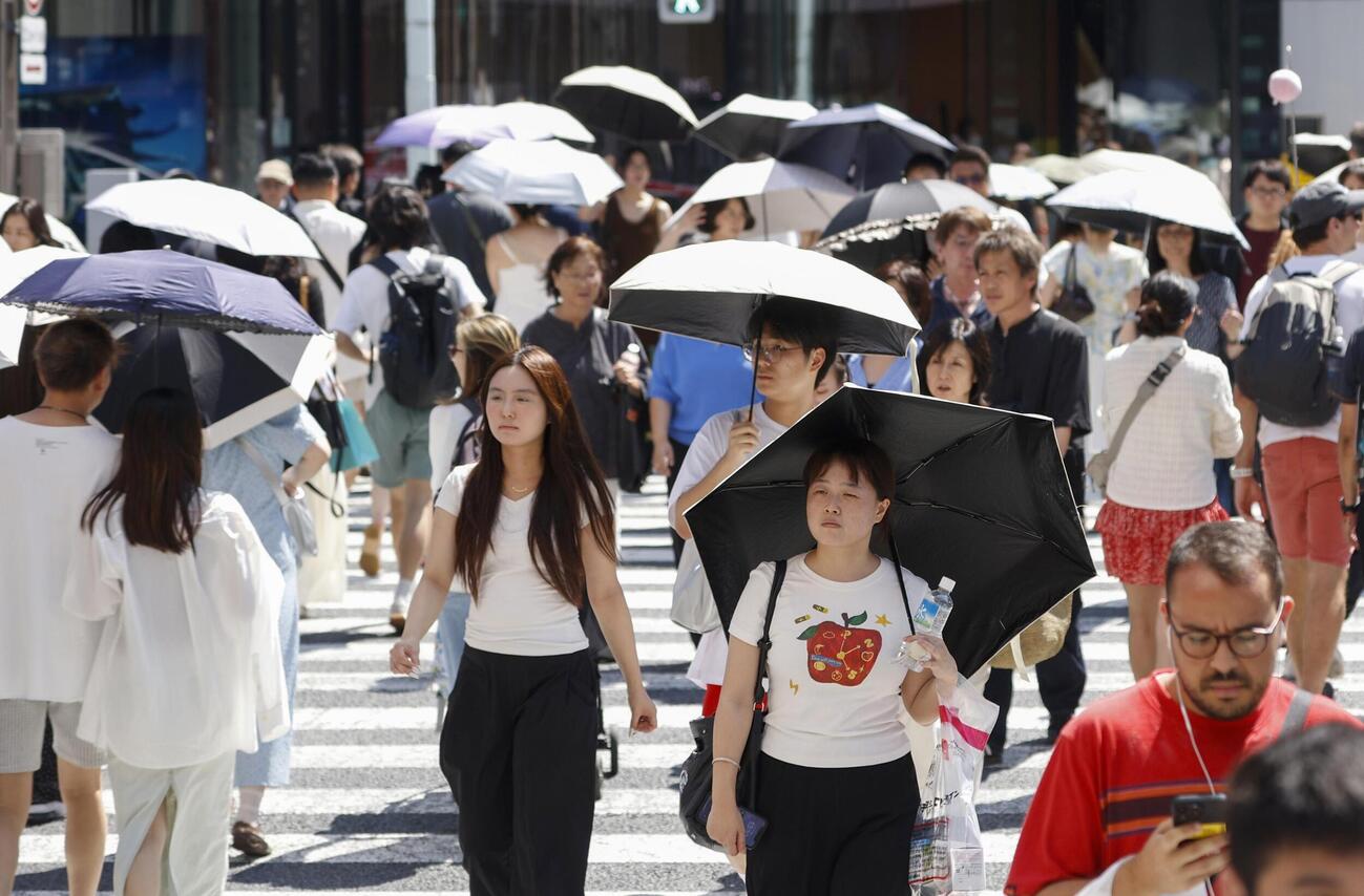 今年初の猛暑日となった東京・銀座を日傘を差して歩く人たち。気象庁は東海、関東甲信が梅雨明けしたとみられると発表した（共同）