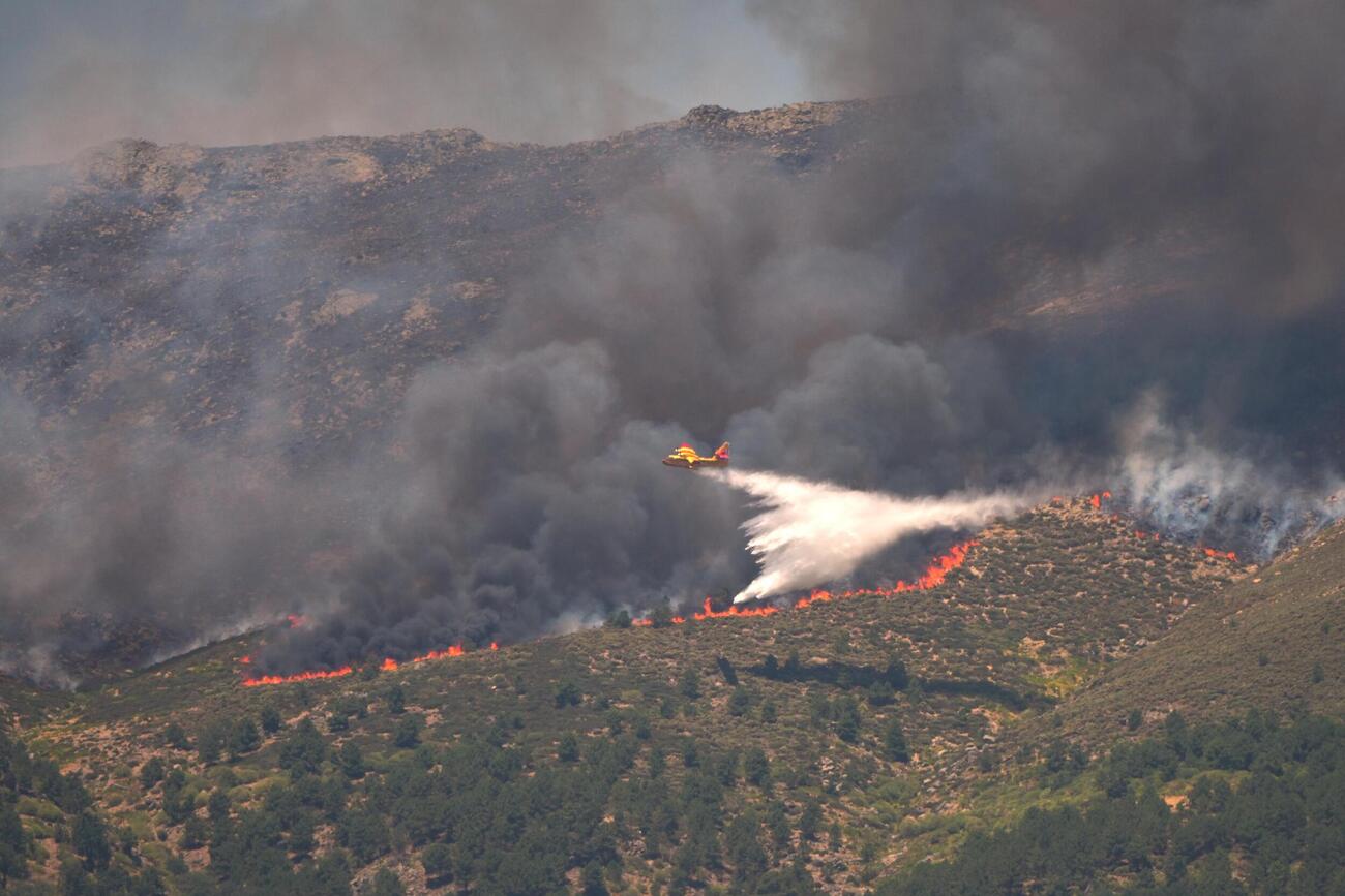 24日、スペイン・アビラ県の山火事現場で水を投下する航空機（AP＝共同）