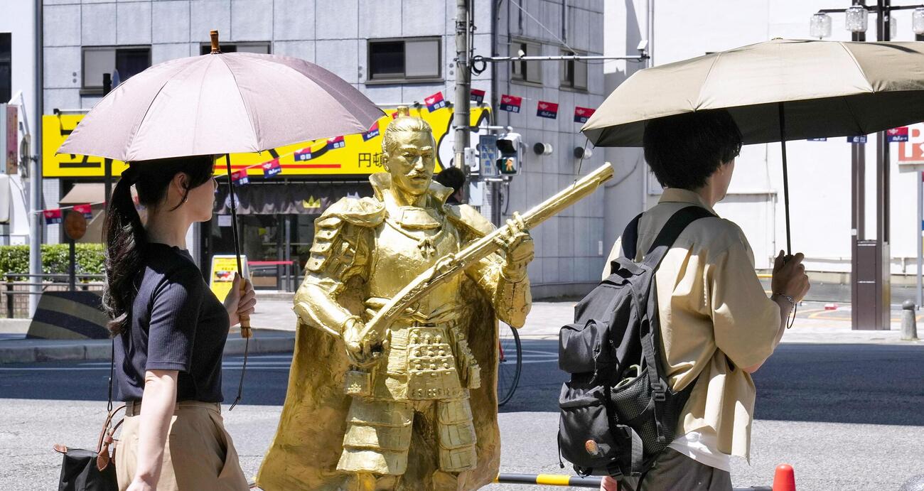 厳しい暑さとなった名古屋市で日傘を差して歩く人たち。奥は織田信長像(共同)