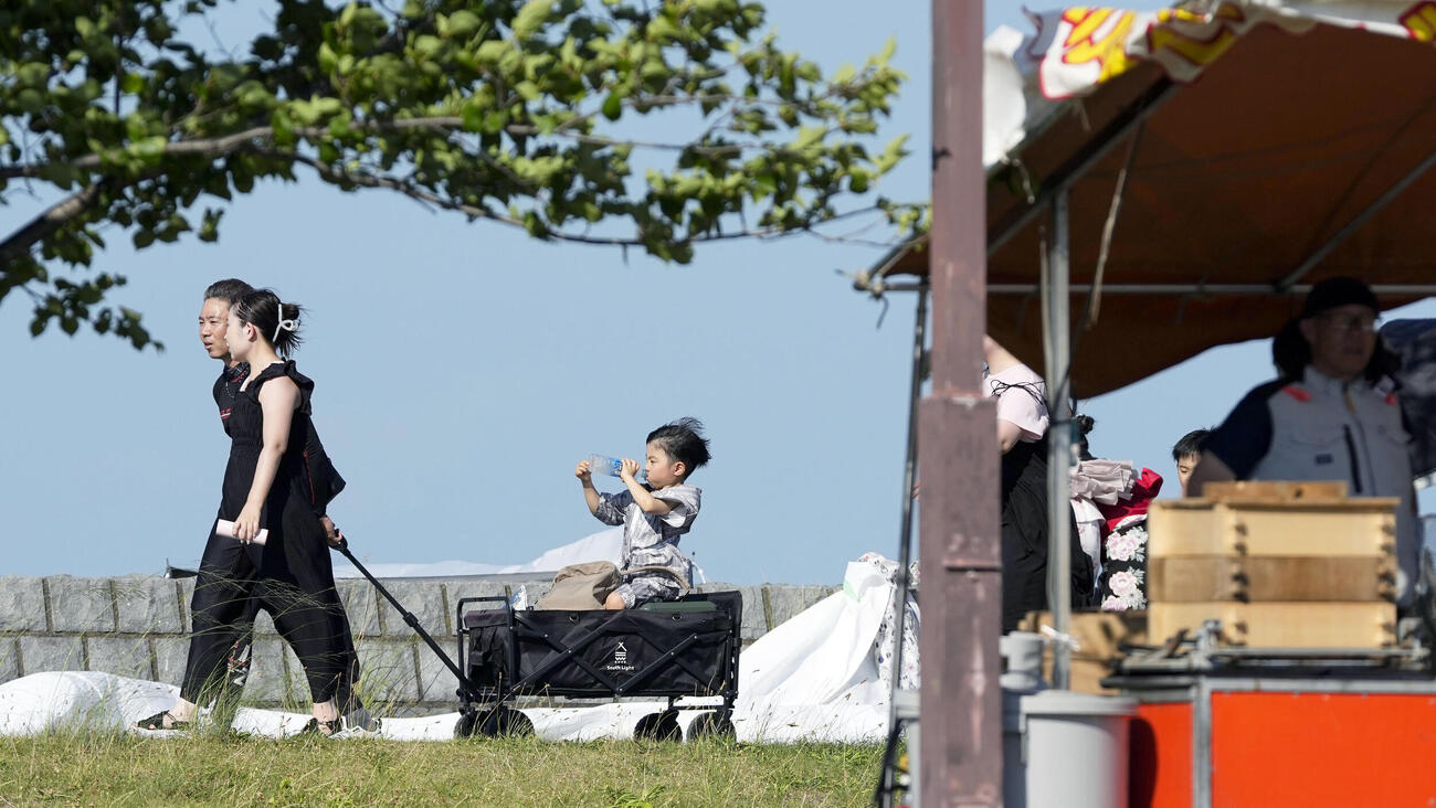 酷暑日となった三重県桑名市で、花火大会の会場周辺を歩く人たち＝25日午後(共同)