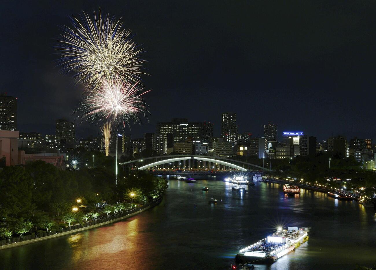 奉納花火が夜空を彩り、大川を船が行き交う天神祭の「船渡御」＝25日夜、大阪市(共同)