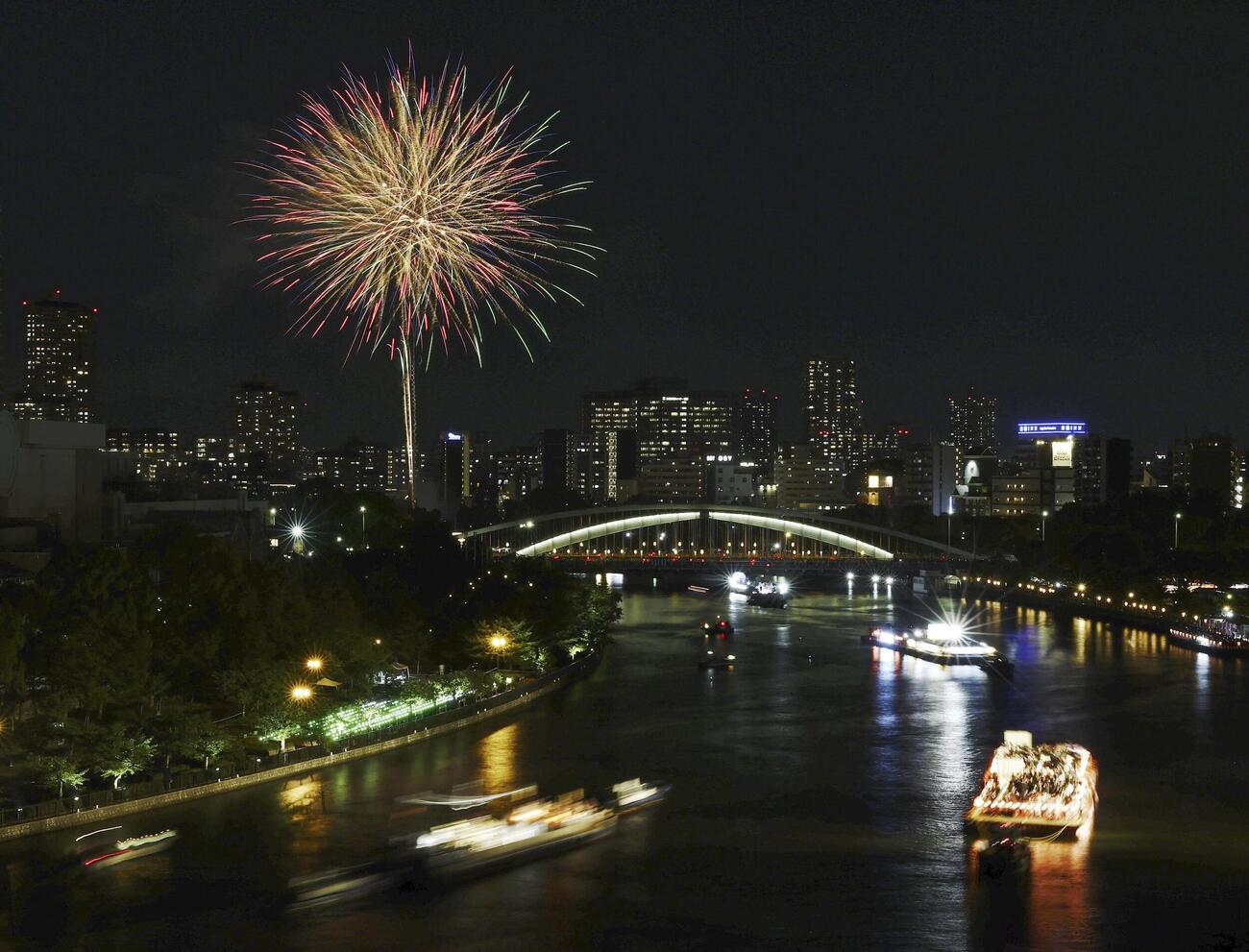 奉納花火が夜空を彩り、大川を船が行き交う天神祭の「船渡御」＝25日夜、大阪市(共同)