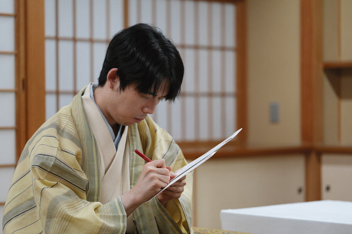 伊藤匠2冠の封じ手が入った封筒にサインをする藤井聡太王位（日本将棋連盟提供）