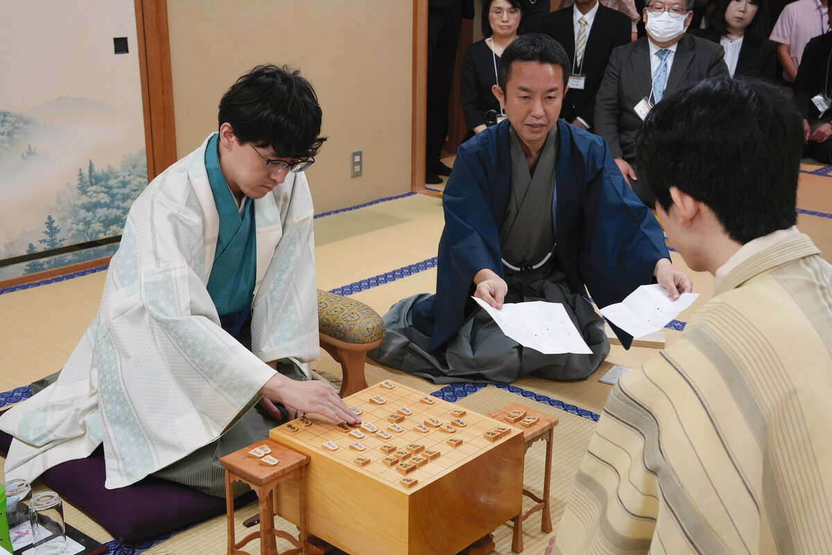 伊藤匠2冠（左）の封じ手を立会人の屋敷伸之九段（中央）が読み上げて王位戦第3局は2日目がスタート（右は藤井聡太王位、日本将棋連盟提供）