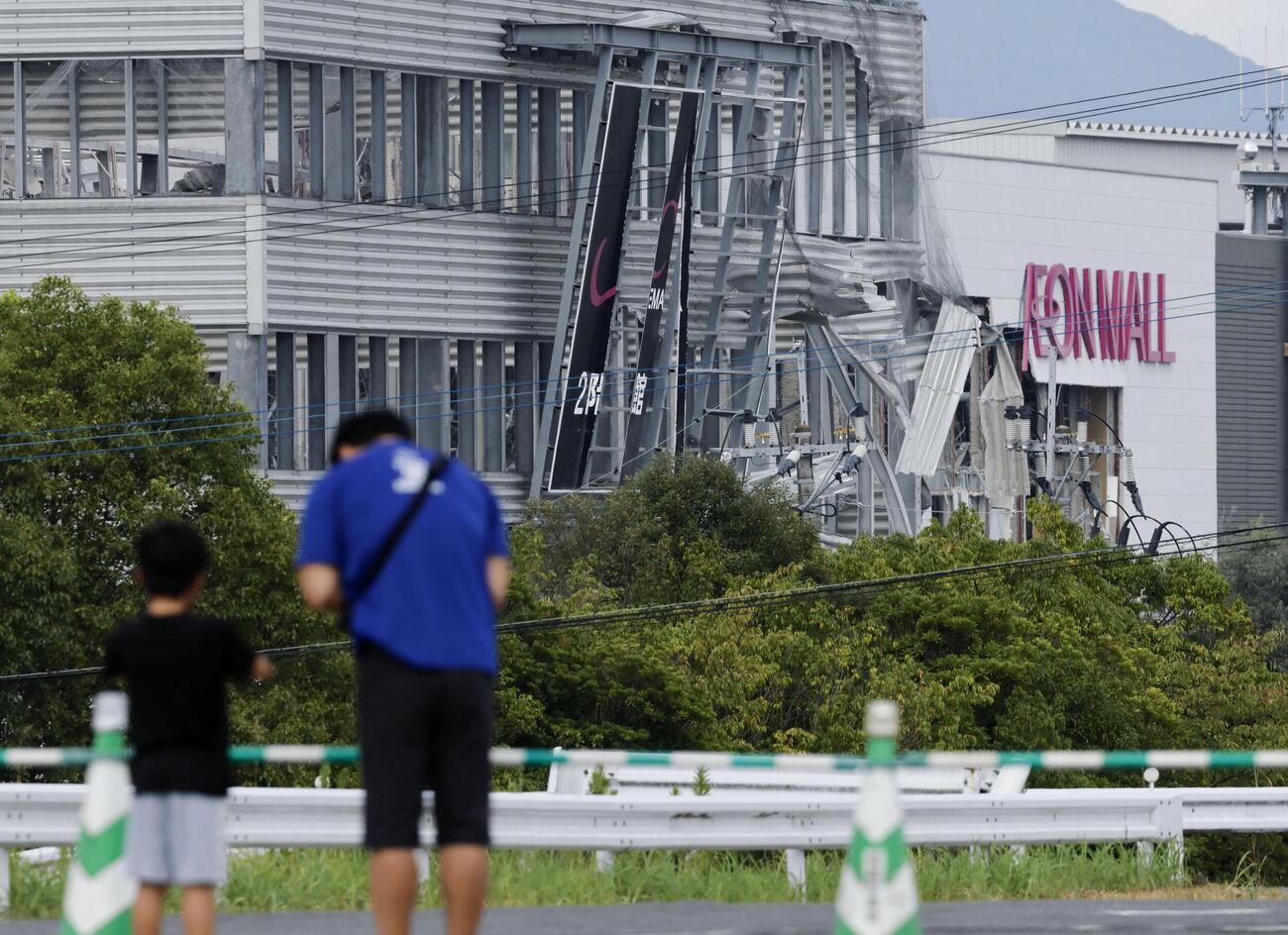地震後の爆発から1週間となった「イオンモール熊本」。外壁が吹き飛んだ建物に向かって手を合わせる親子の姿があった＝4日午後、熊本県嘉島町（共同）