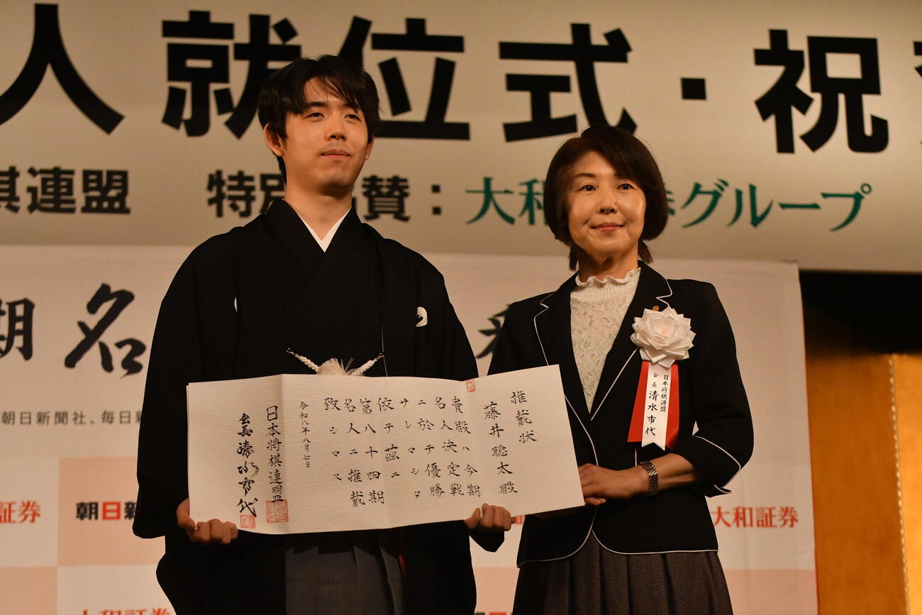 藤井聡太名人（左）は日本将棋連盟の清水市代会長（右）から推戴状を贈られる