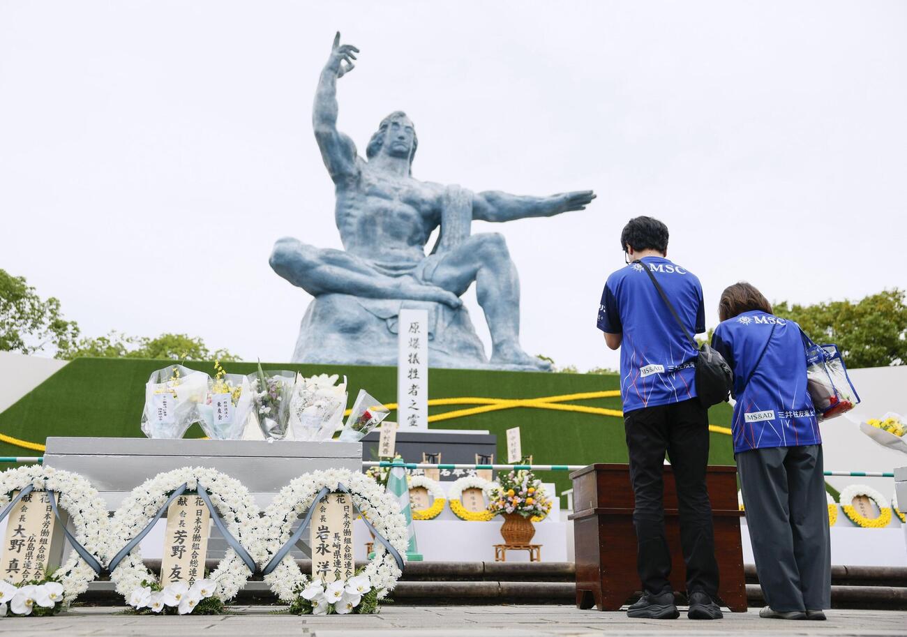 長崎市の平和公園を訪れ、平和祈念像の前で手を合わせる人たち（共同）