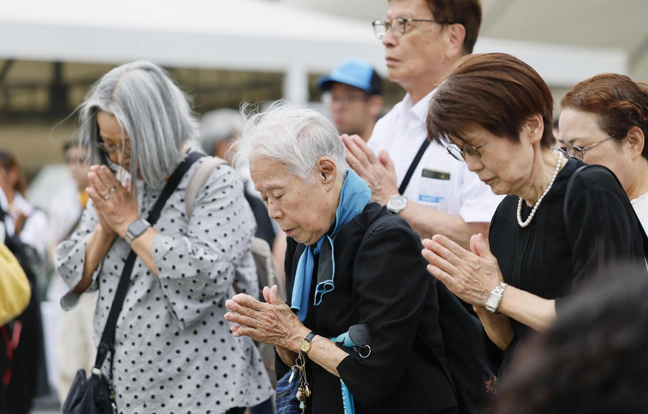 長崎市の平和公園を訪れ、平和祈念像の前で手を合わせる人たち（共同）