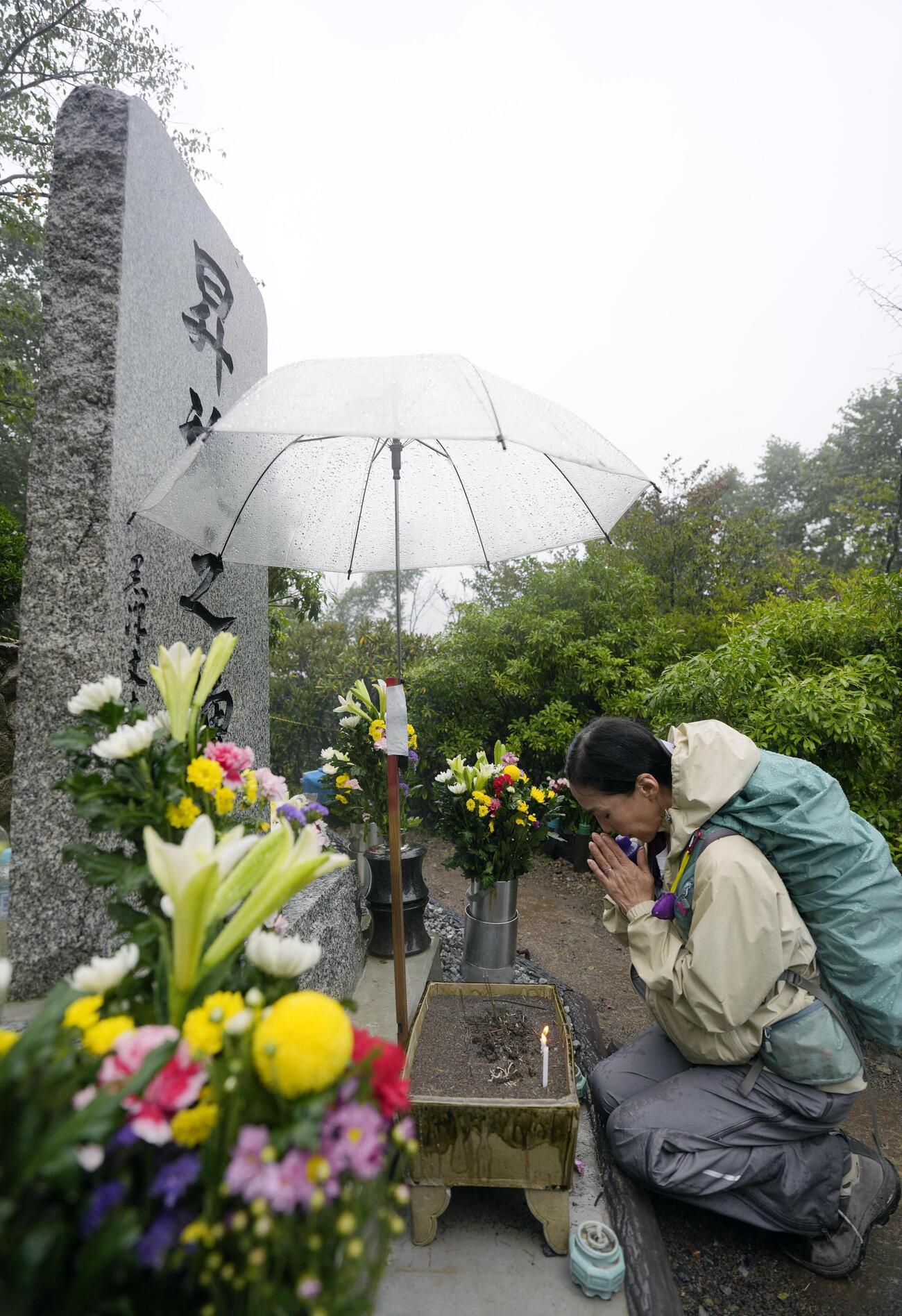 日航機墜落事故現場の尾根に立つ「昇魂之碑」で手を合わせる人＝12日午前、群馬県上野村（共同）