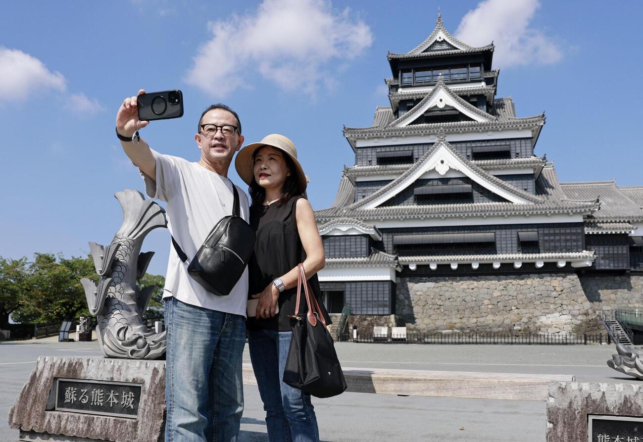 地震発生以来初めて開園した熊本城の天守閣を背に写真を撮る来園者＝13日午前、熊本市（共同）