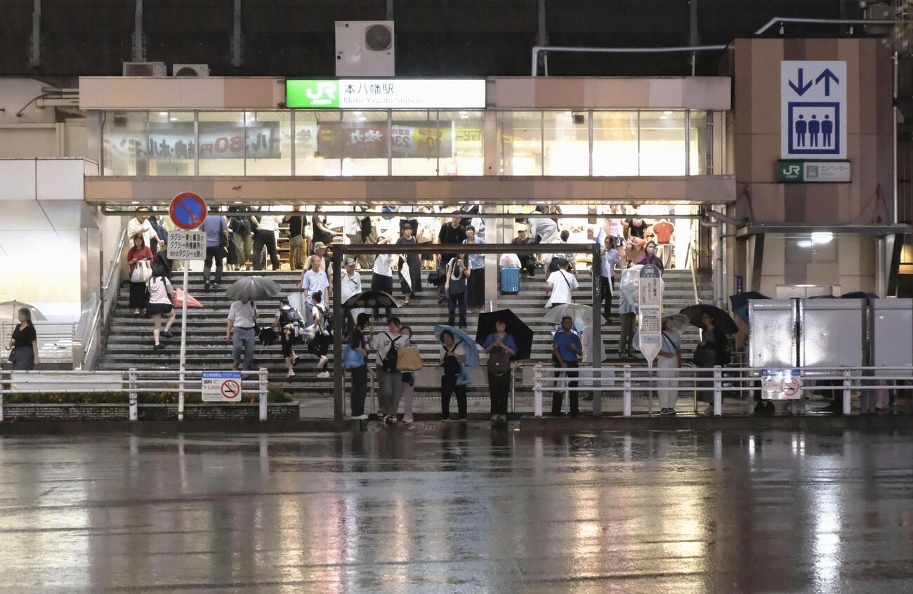 降りしきる雨の中、JR本八幡駅で雨宿りする人たち（共同）