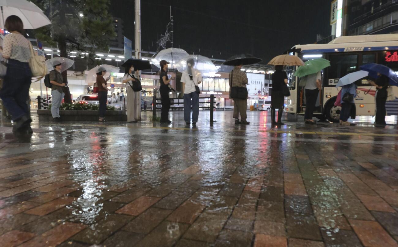 降りしきる雨の中、JR本八幡駅前でバスを待つ人たち＝13日午後7時2分、千葉県市川市（共同）