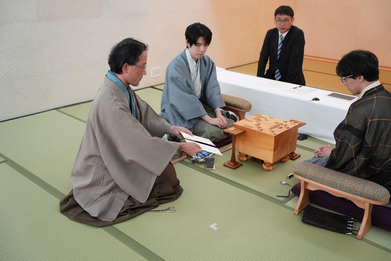 立会人の深浦康市九段（左）が手にする封じ手の封筒を確認する藤井聡太王位（中央）、伊藤匠2冠（日本将棋連盟提供）2026年8月19日、長崎市、外部提供