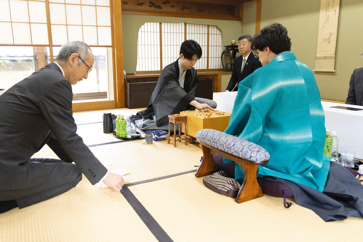 立会人の中田功八段（左）が封じ手を開封して藤井聡太王位（中央）に伊藤匠2冠（右）が挑む王位戦第5局は2日目が再開された（日本将棋連盟提供）