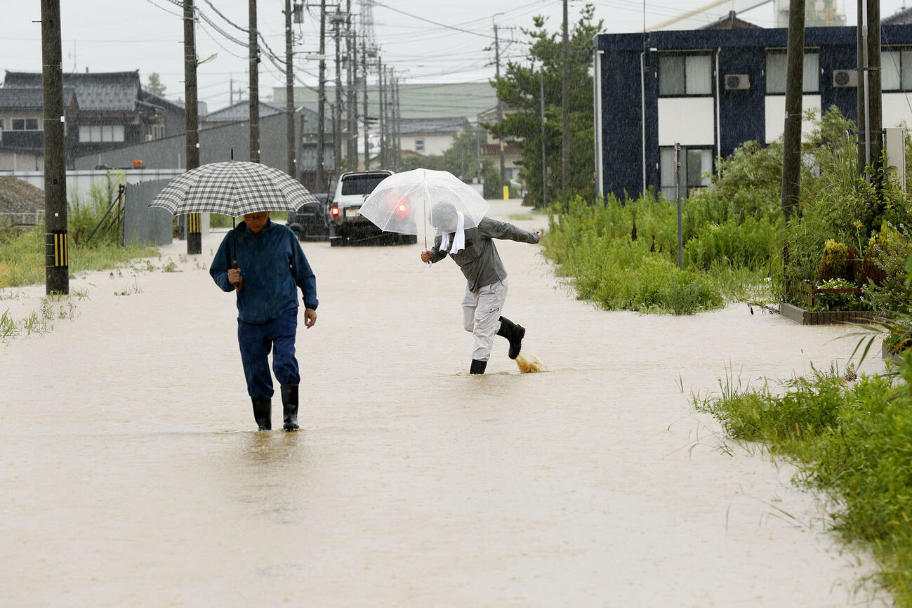 大雨で冠水した石川県羽咋市で道路を歩く人たち（共同）
