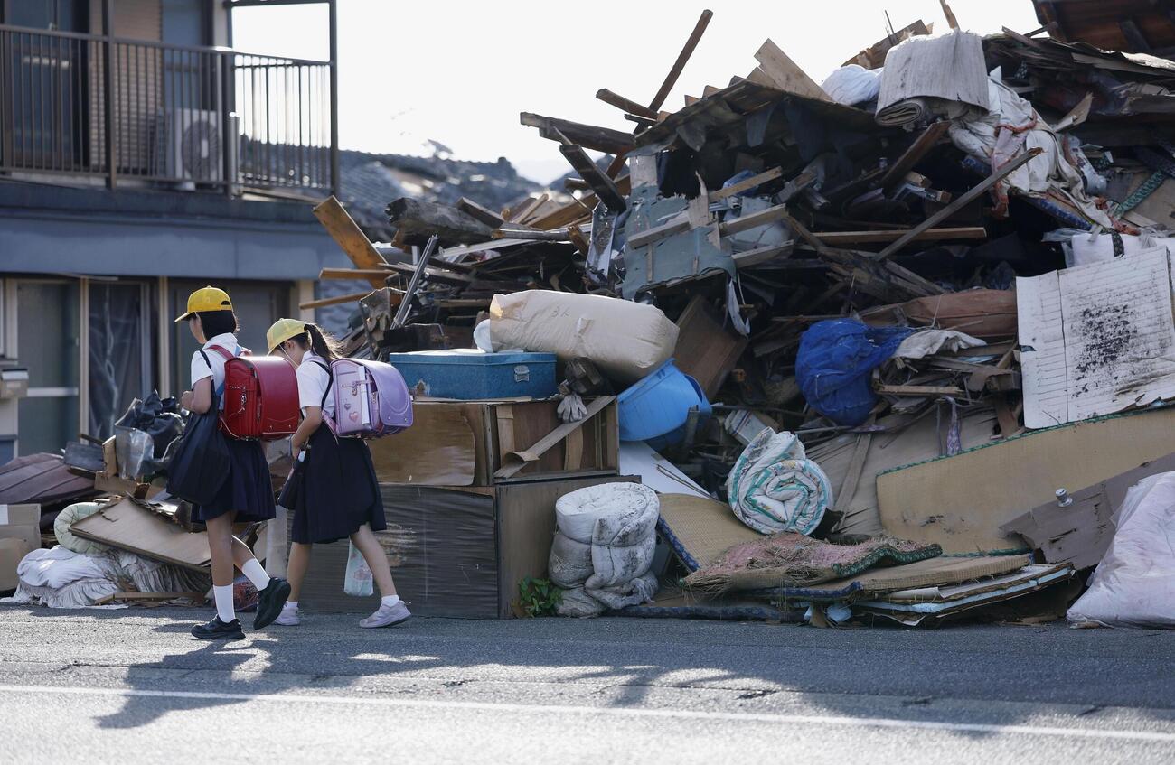 がれきの脇を歩いて小学校に登校する児童＝28日午前、熊本県八代市（共同）