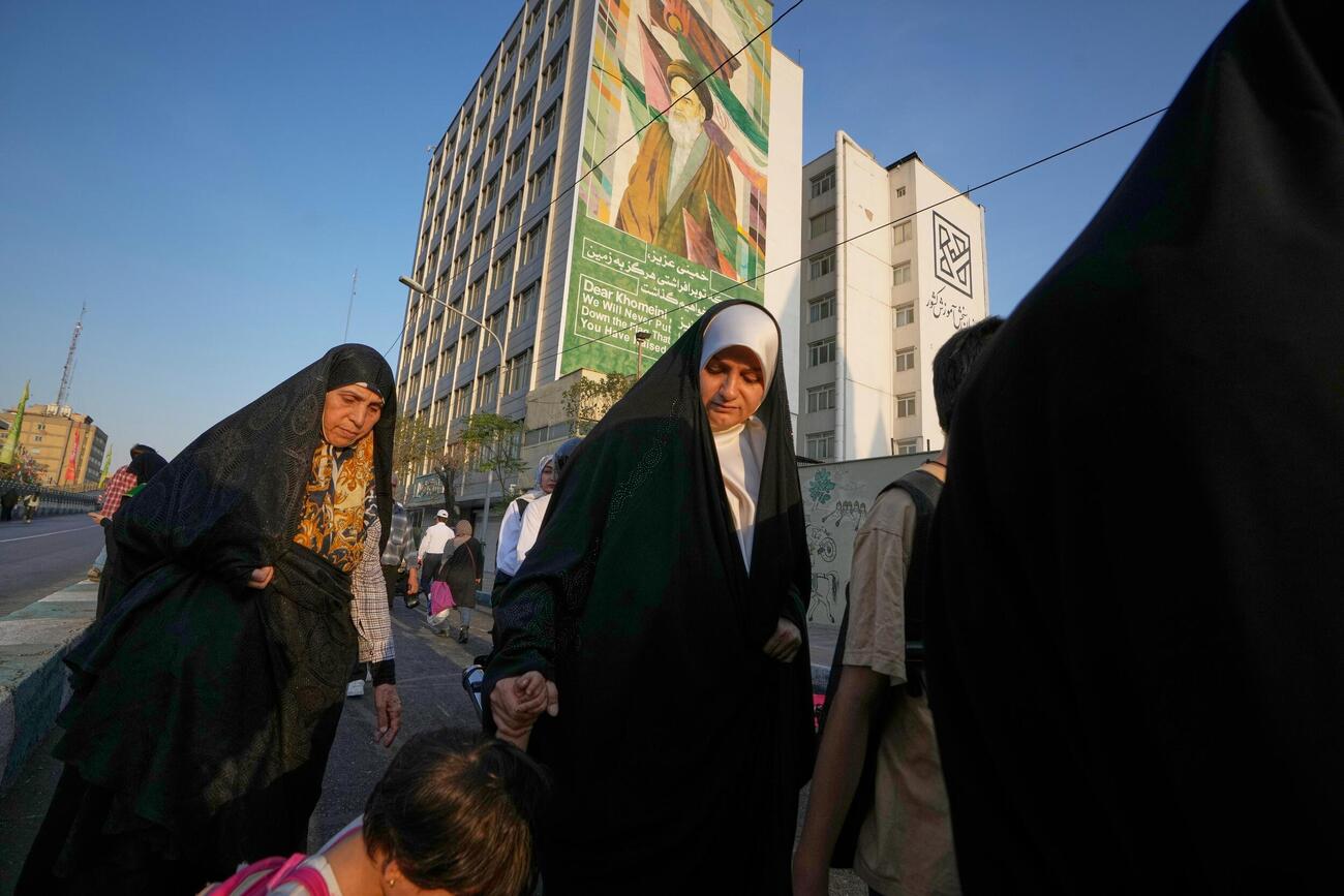 イラン革命の指導者ホメイニ師を描いた看板の前を通る女性（AP＝共同）