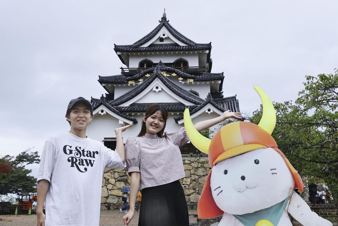 世界文化遺産登録を目指す推薦候補に選ばれた滋賀県彦根市の彦根城を背に、記念撮影する観光客。右は市のキャラクター「ひこにゃん」のパネル（共同）