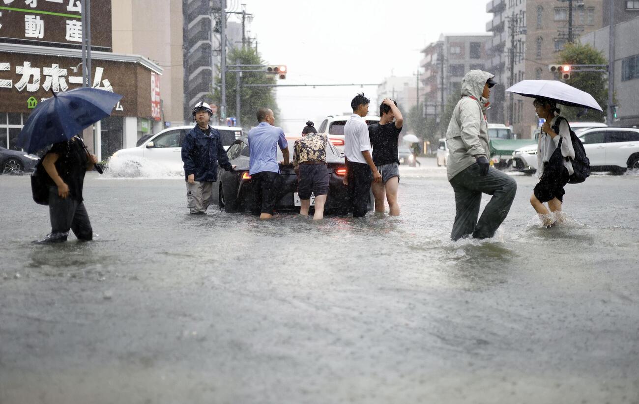 大雨で水があふれた名古屋市瑞穂区の道路。男性らが立ち往生した車を押していた（共同）