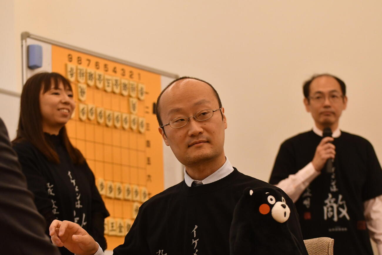 熊本県PRマスコットキャラクターのくまモンを手に登場した渡辺明九段（中央）