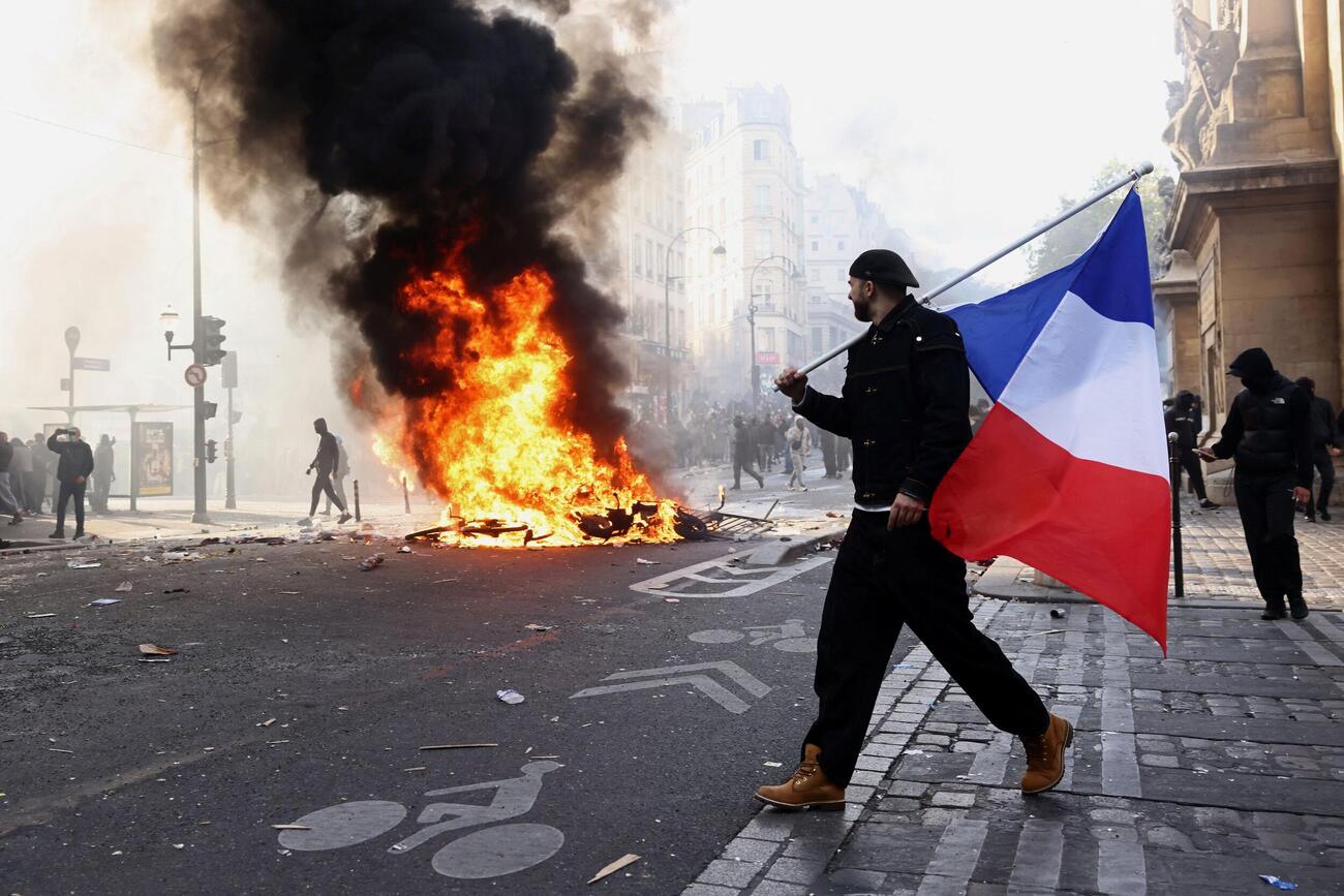 炎が上がるパリでフランス国旗を持つデモ参加者（ロイター）