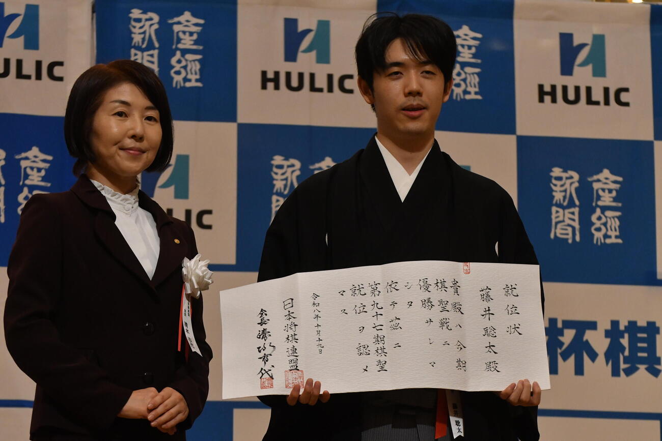 日本将棋連盟・清水市代会長（左）から渡された就位状を持つ藤井聡太棋聖（右）