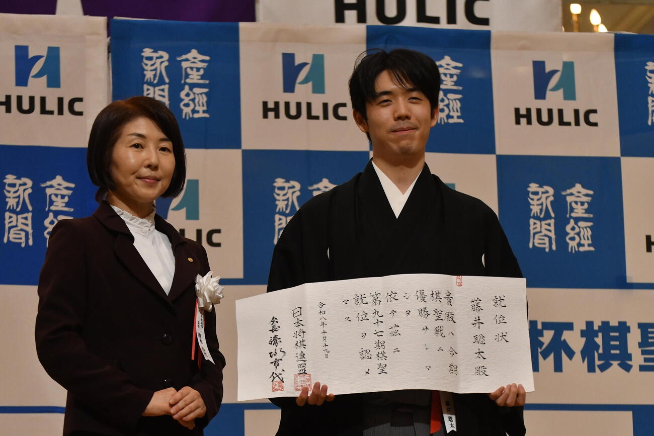 日本将棋連盟・清水市代会長（左）から渡された就位状を持つ藤井聡太棋聖（右）
