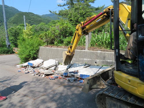 鶴岡市湯温海の山中で、亀裂が入った道路上に散乱した、倒壊した塀を撤去する作業員（撮影・村上幸将）