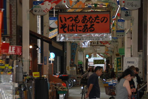 京アニ作品「たまこまーけっと」の舞台のモデルとなった出町桝形商店街（京都市上京区）には作品から逆輸入された「いつもあなたのそばにある」のメッセージを掲げる看板がある（撮影・松浦隆司）