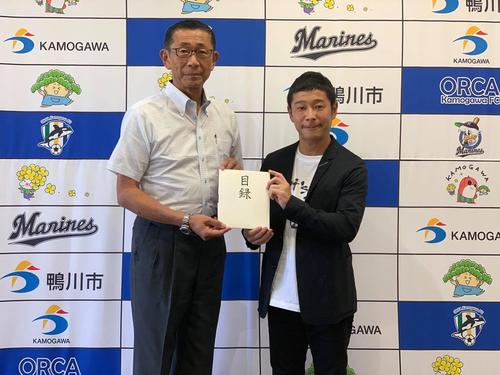 鴨川市の亀田郁夫市長（左）に目録を手渡した前澤友作氏