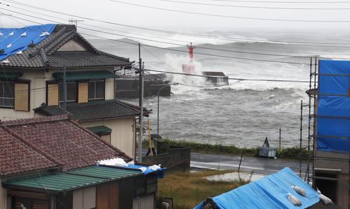 千葉県館山市で、台風19号の影響で打ち寄せる波。手前は屋根にブルーシートを掛けられた家屋（共同）