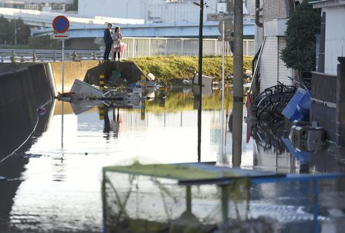 13日午前6時15分、川崎市　台風19号の影響で冠水した道路脇で立ち尽くす人（共同）