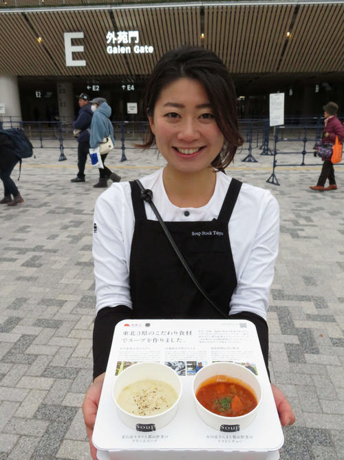 国立競技場オープニングイベント開演前、敷地内の復興庁PRブースで配布された東日本大震災被災3県産食材を使用したスープ2種。笑顔でスープセットを来場者に配布した「スープストックトーキョー」商品部の松尾琴美さん（撮影・近藤由美子）
