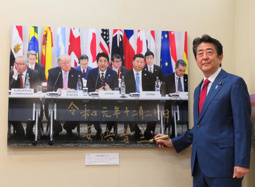 報道写真展の視察に訪れた安倍首相はサインを終え写真に納まる（撮影・佐藤勝亮）