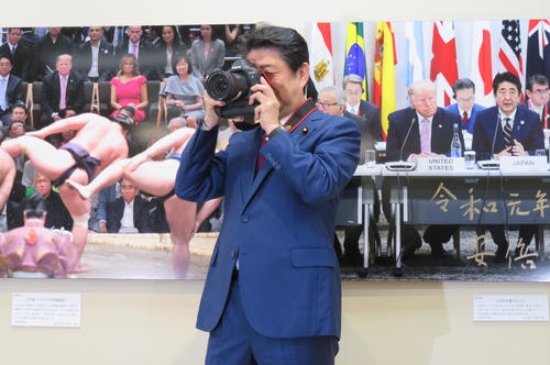 報道写真展の視察に訪れた安倍首相はカメラを渡され、集まった報道陣を連写撮影する（撮影・佐藤勝亮）