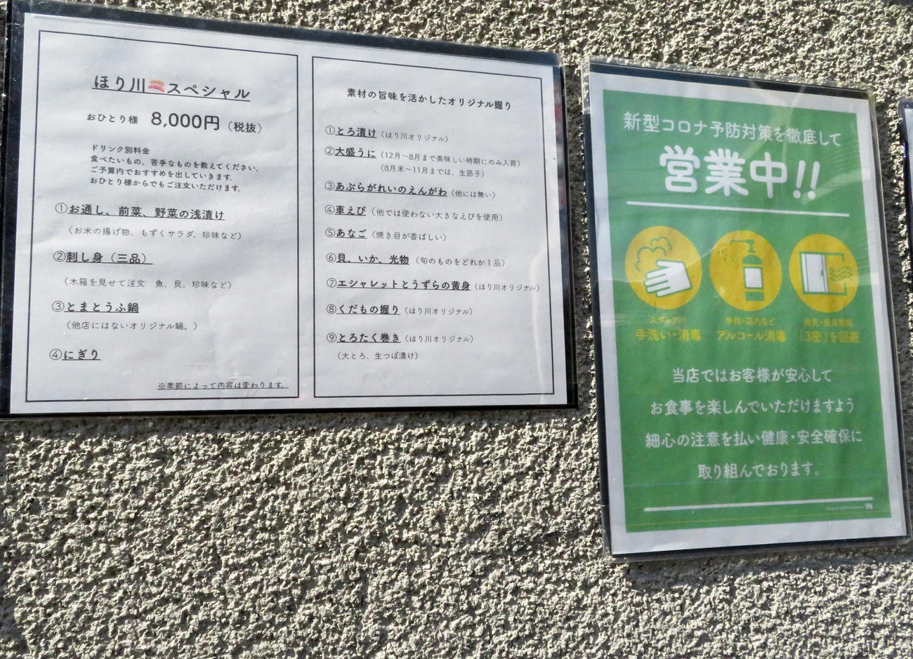 「鮨ほり川」の外壁には、コロナ予防対策を講じて営業中の張り紙や約1カ月の営業自粛期間中に考案した新コースを記した張り紙などがあった（撮影・近藤由美子）