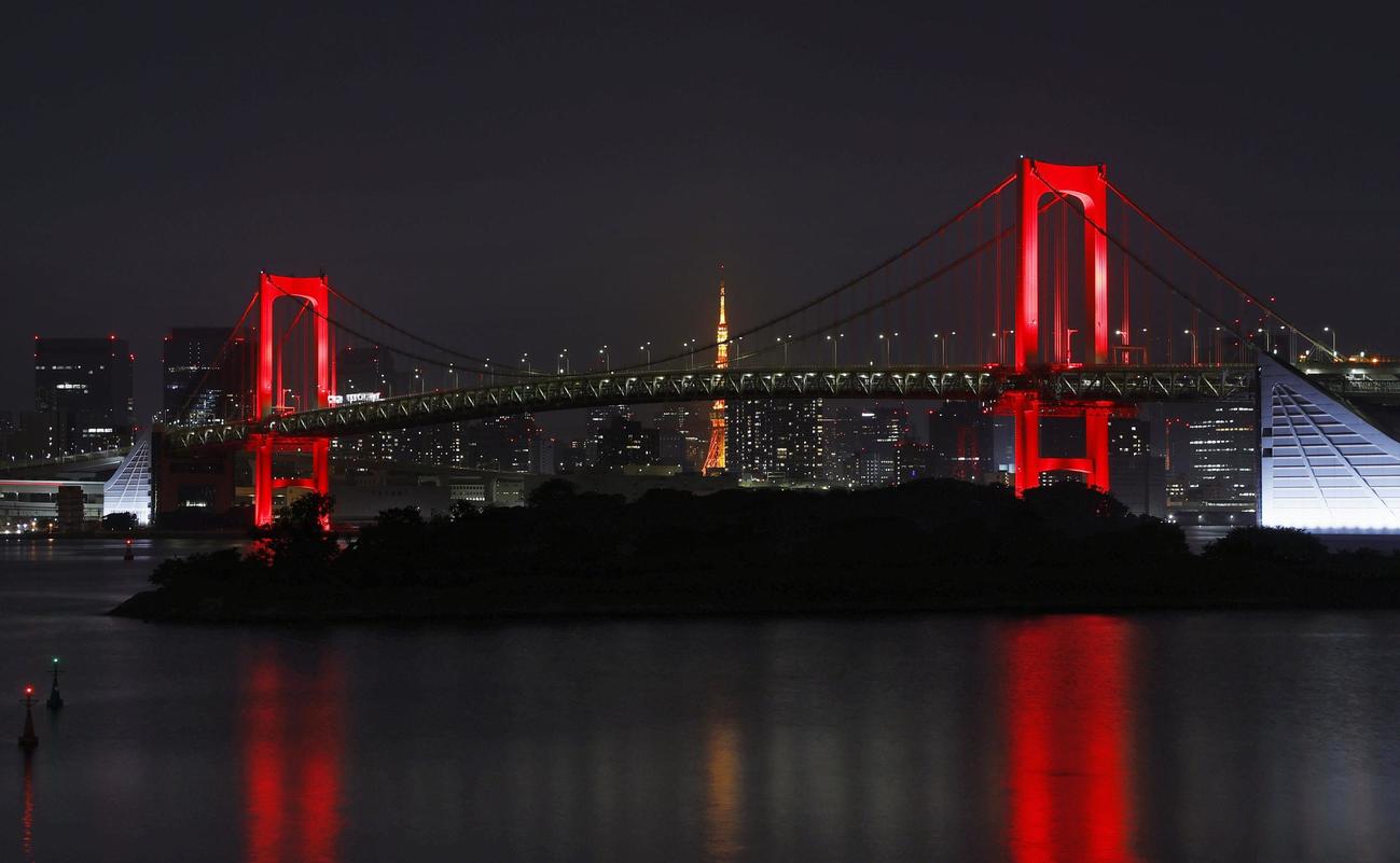 初の「東京アラート」が発令され、赤く点灯された東京湾に架かるレインボーブリッジ。後方中央は東京タワー＝2日深夜（共同）