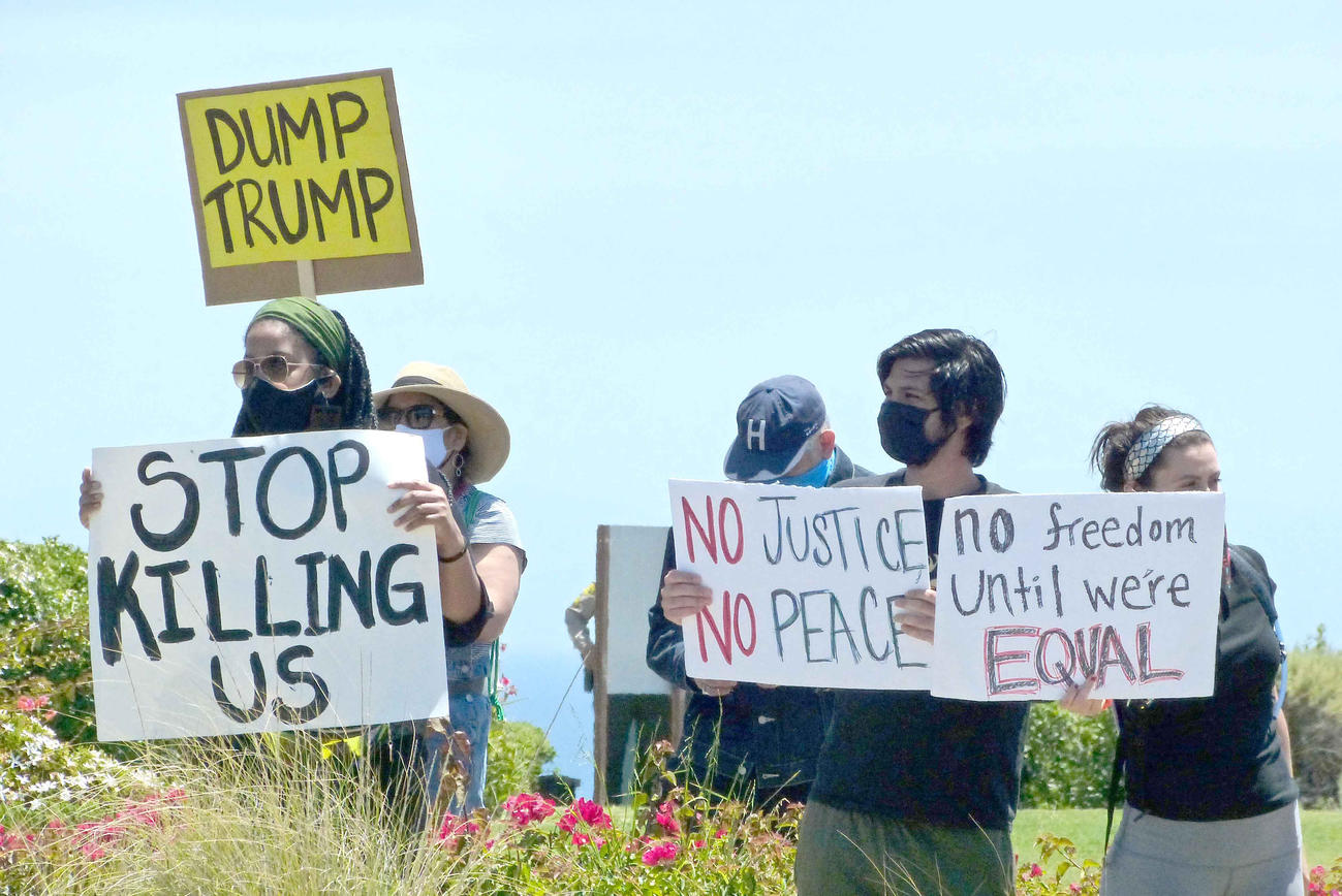 プラカードを手にトランプ・ナショナル・ゴルフ・クラブの前で抗議する人々