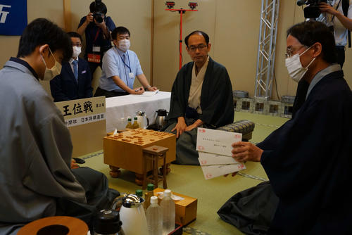 藤井聡太七段（左）は立会人の深浦康市九段（右）が持つ封じ手の封筒3通を確認する（中央は木村一基王位、日本将棋連盟提供）