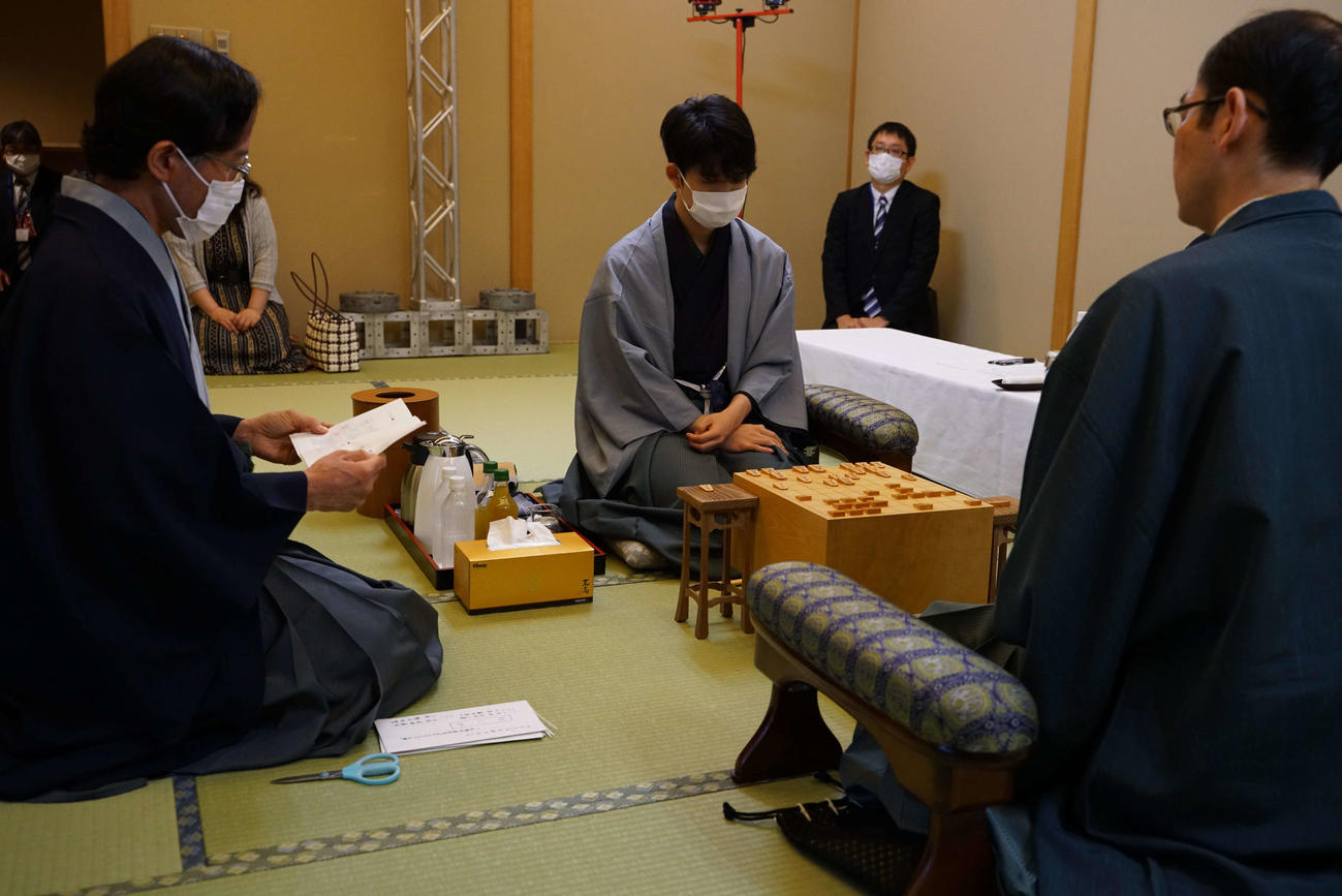 藤井聡太七段（中）は立会人の深浦康市九段（左）が読み上げる封じ手を確認する（右は木村一基王位、日本将棋連盟提供）