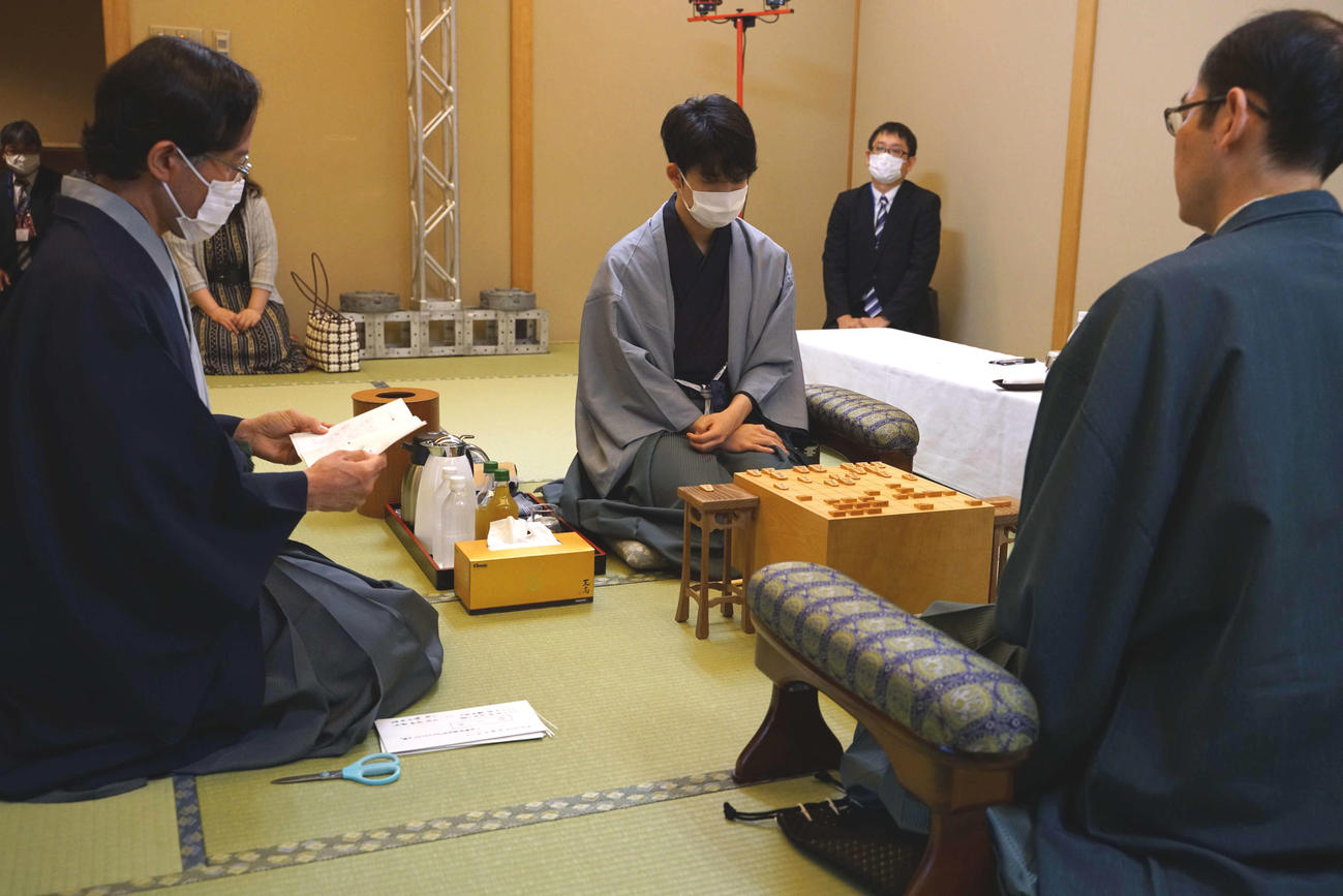 藤井聡太七段（中央）は立会人の深浦康市九段（左）が読み上げる封じ手を確認する。右は木村一基王位（日本将棋連盟提供）