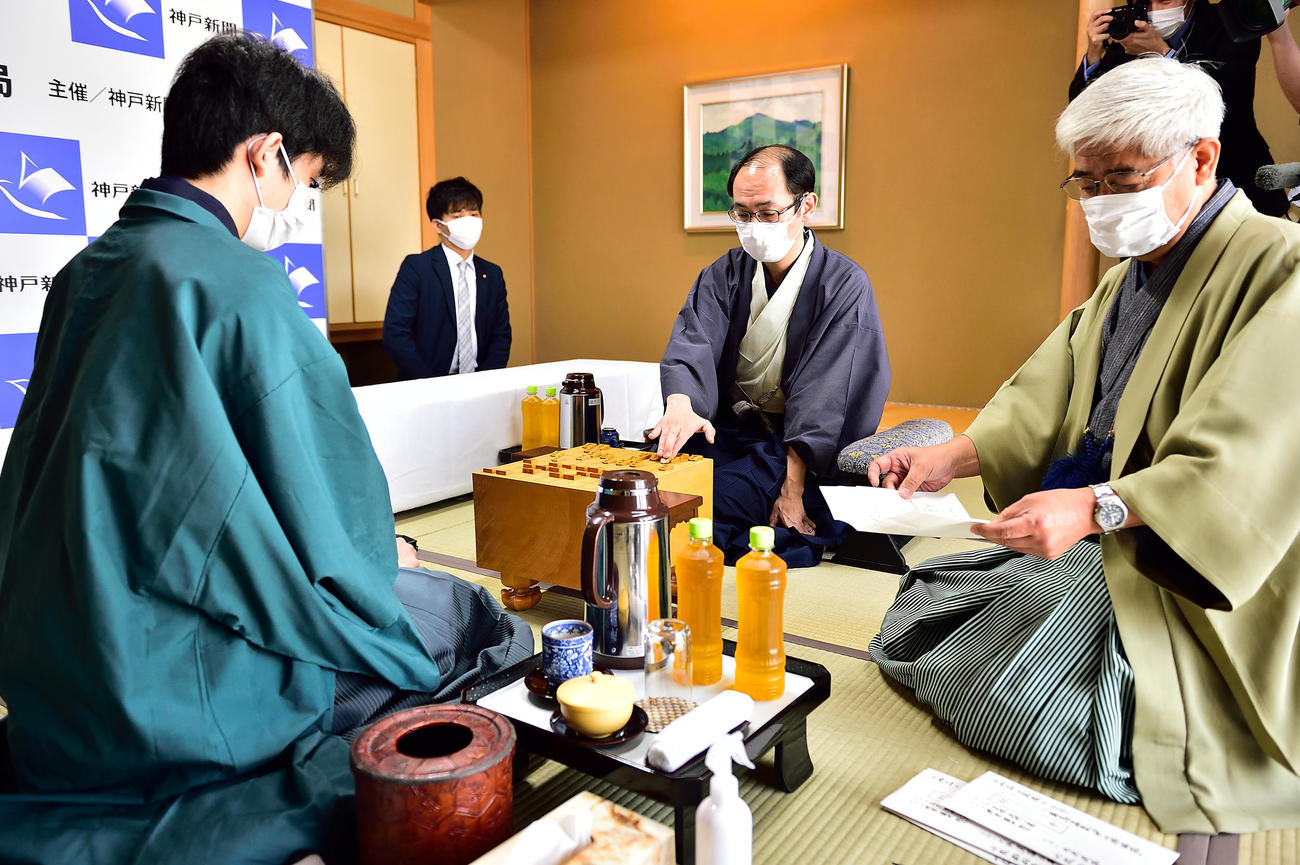 立会人の淡路仁茂九段（右）が封じ手を読み上げ、封じ手を指す木村一基王位（中央）。左は藤井聡太棋聖（日本将棋連盟）
