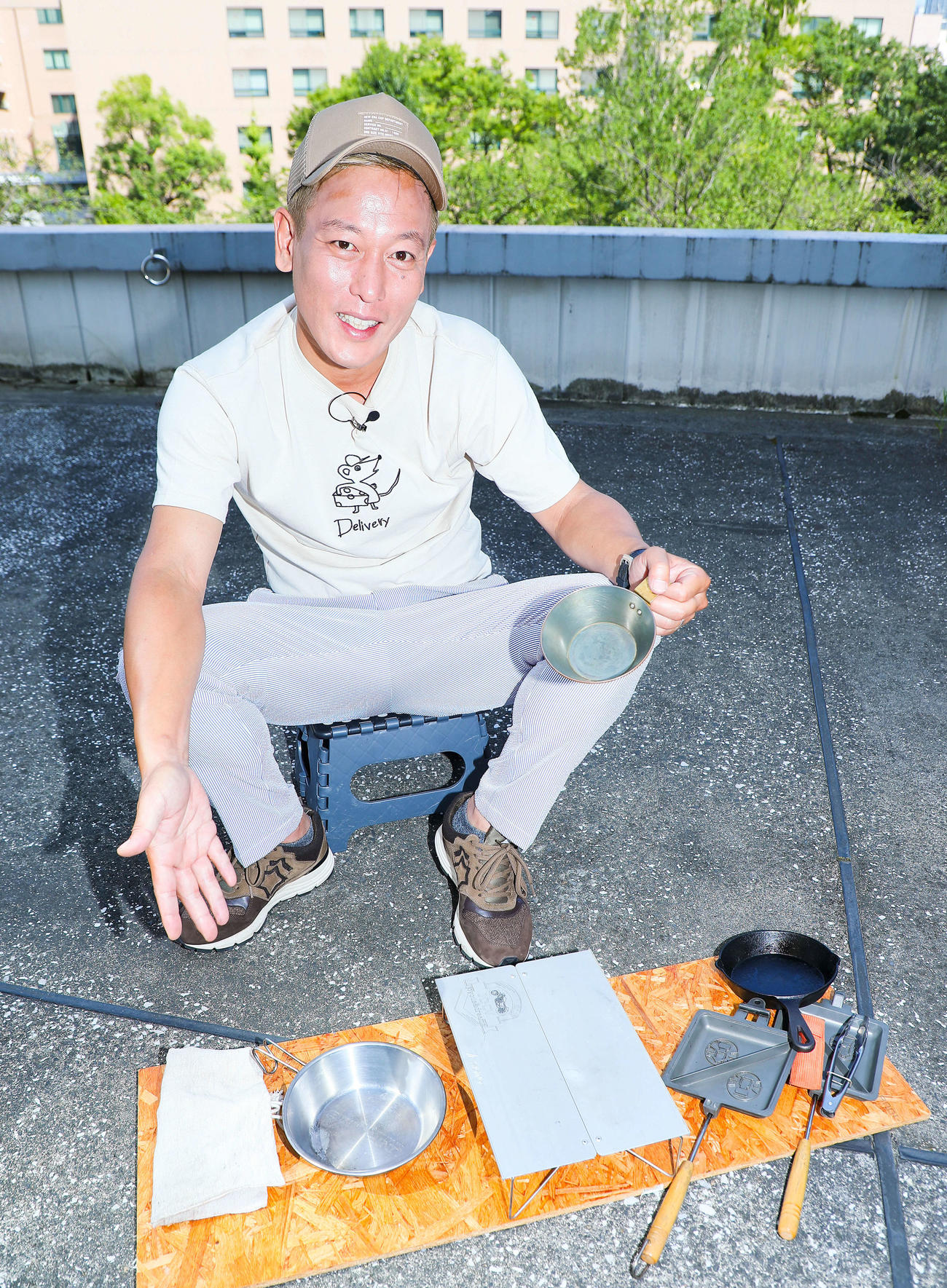 お気に入りのシェラカップを手に、他大事に使い込んでいるキャンプギアを並べ写真に納まるじゅんいちダビッドソン（撮影・河田真司）　