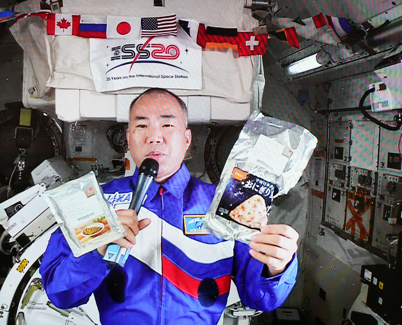 滞在中の国際宇宙ステーションから記者会見に応じる宇宙飛行士の野口聡一さんは宇宙食を披露する（撮影・江口和貴）