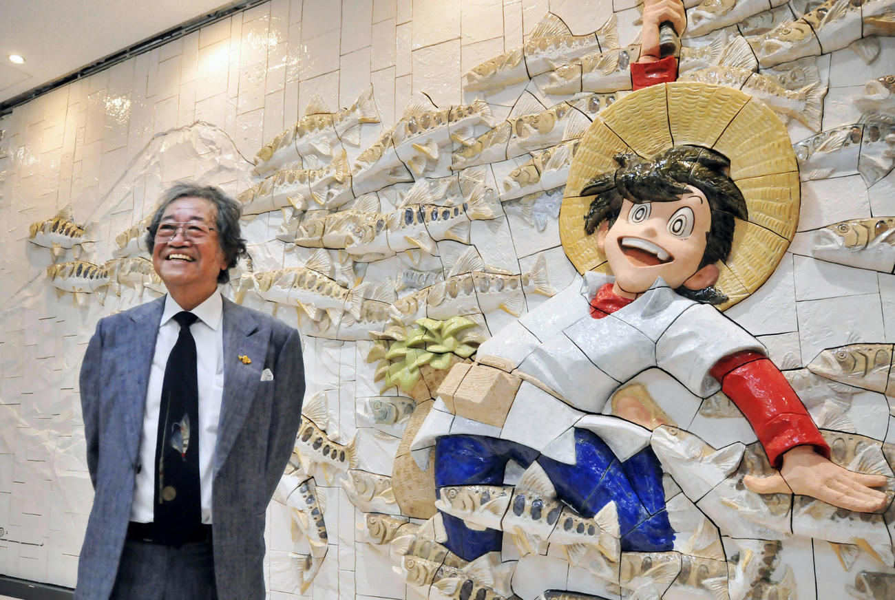 「釣りキチ三平」のレリーフの前で笑顔の矢口高雄さん＝2016年10月、秋田空港（共同）