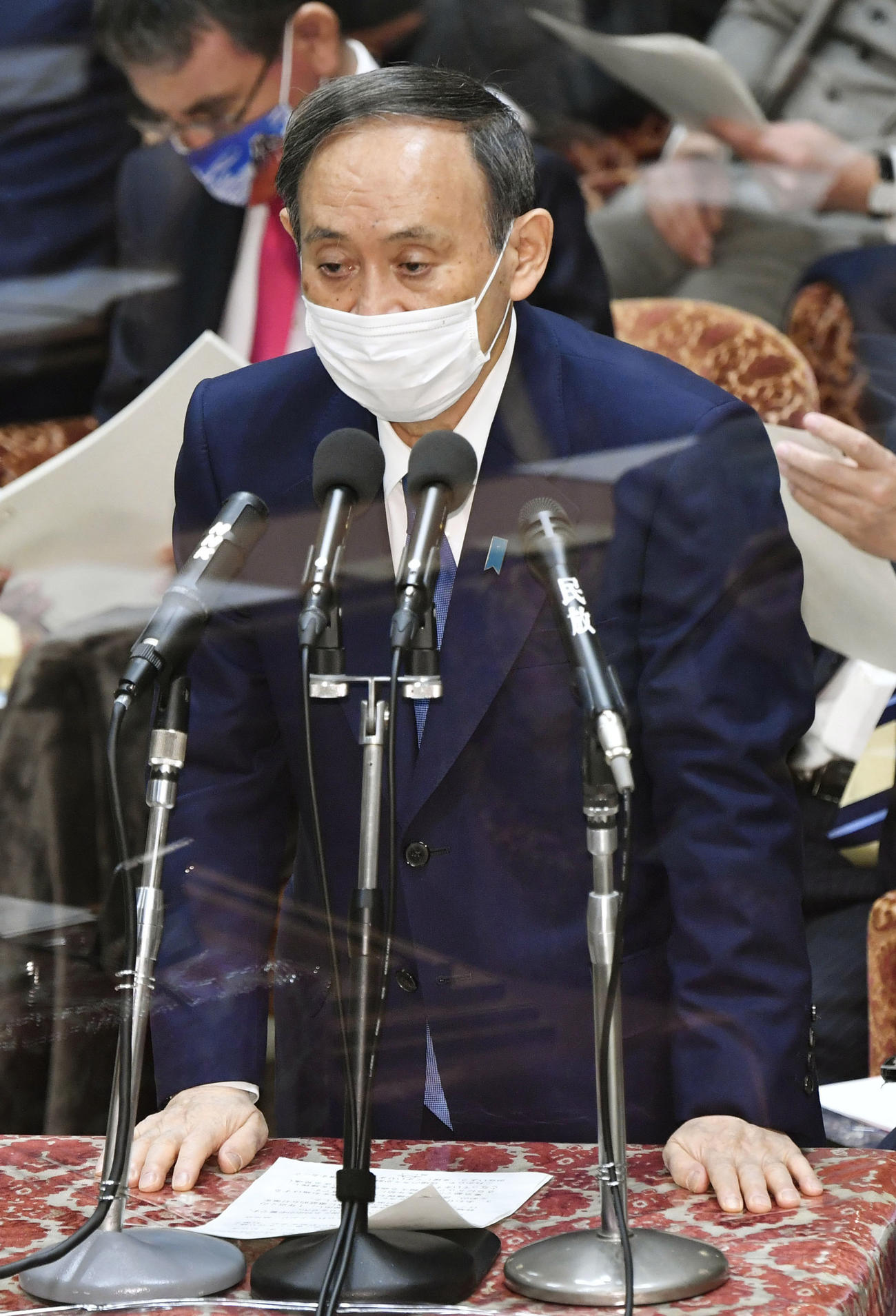 新型コロナ感染対策で置かれたアクリル板越しに、衆院予算委で答弁する菅首相（共同）